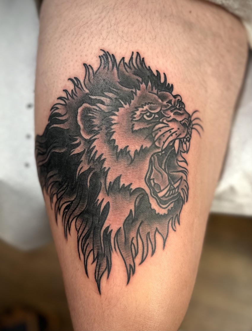 Black and gray lion tattooed on the thigh.